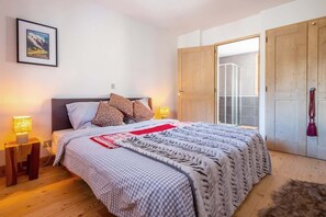 A bedroom with a bed, two bedside lamps, a framed picture on the wall, and a wooden wardrobe.