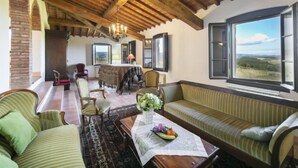 A spacious living area with a high wooden ceiling, a dining table with chairs, a sofa, and a view of the countryside through large windows. - Vedi Torre by Interhome (San Gimignano)