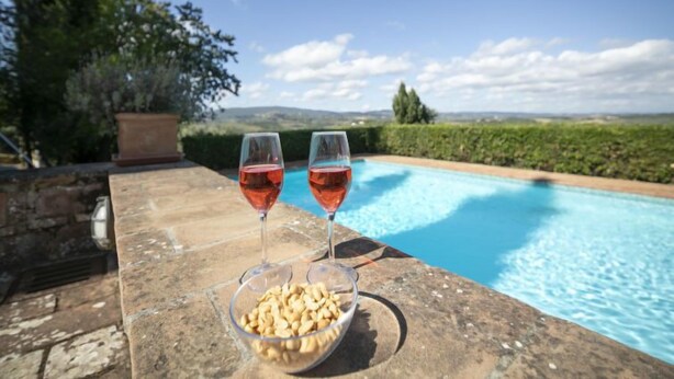 A poolside setting with two glasses of red wine and a bowl of snacks on a stone ledge. - Vedi Torre by Interhome (San Gimignano)