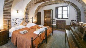 A room with two beds, a wooden bench, a wooden cabinet, and a window with a view. - Vedi Torre by Interhome (San Gimignano)