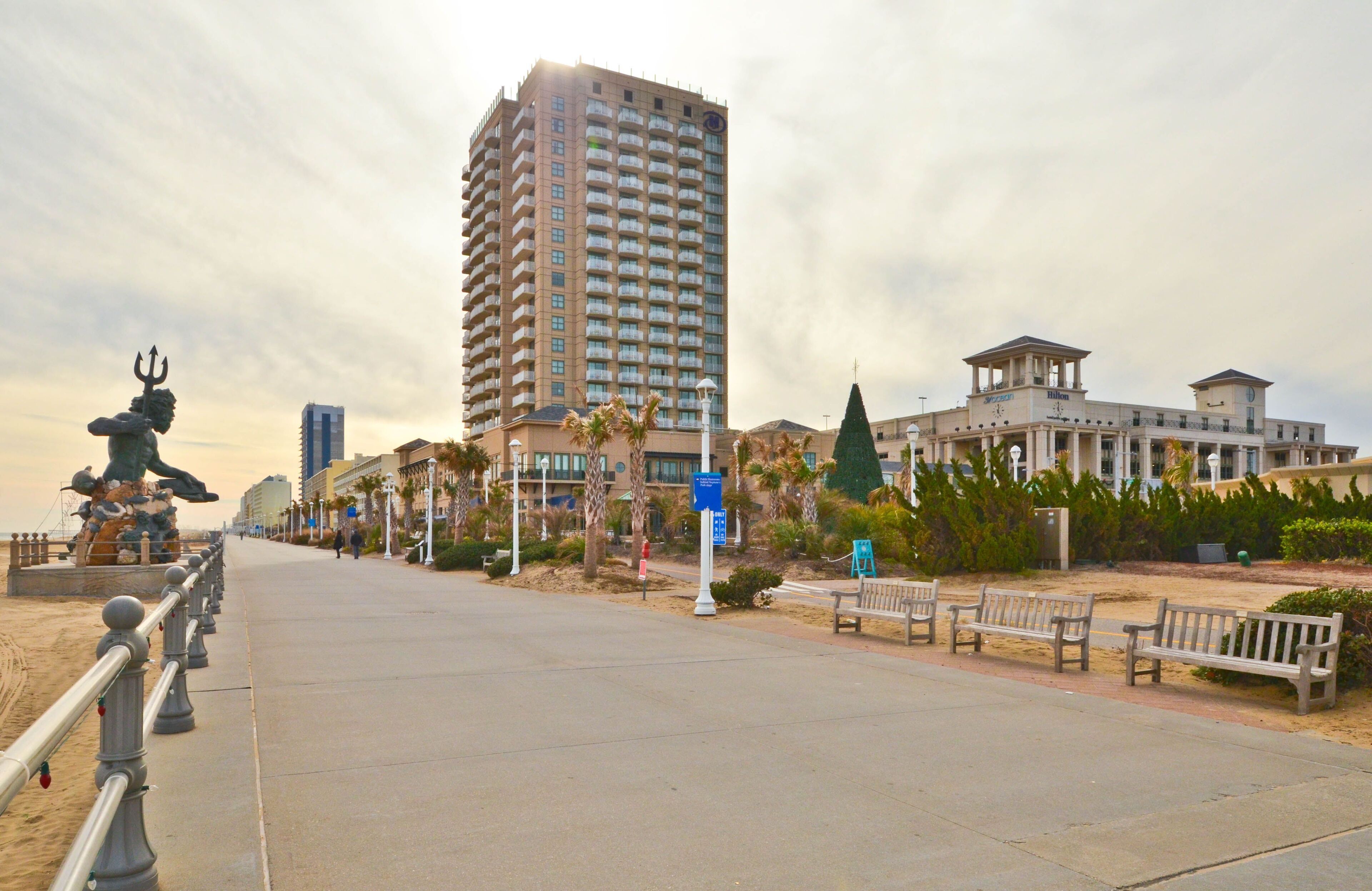 Une promenade en bord de mer, avec un grand hôtel, des bancs et une statue.