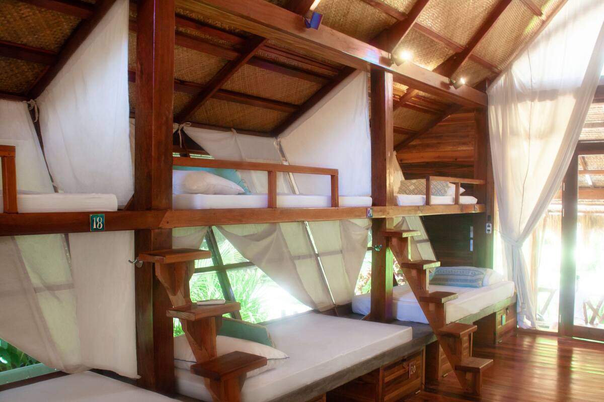 A room with bunk beds, wooden furniture, and a thatched roof.