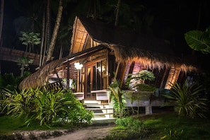 A thatched-roof structure with a wooden porch and steps leading up to it, surrounded by lush greenery. - Harana Surf Resort - Hostel (General Luna)