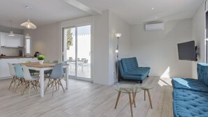 Een moderne woonkamer met een blauwe bank, een glazen salontafel, en een eethoek met een houten tafel en stoelen.