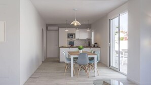 Een moderne keuken met witte kastjes, een houten eettafel en een glazen salontafel.