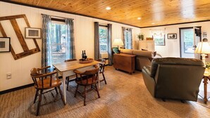 A cozy room with a wooden ceiling, a dining table with chairs, a sofa, and a lamp.