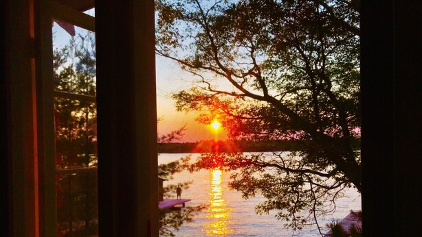 A sunset over a body of water with trees reflected on the surface.