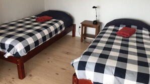 Kaksi erillistä sänkyä, joissa on ruutukuosiset vuodevaatteet, pieni puinen yöpöytä ja lamppu niiden välissä.