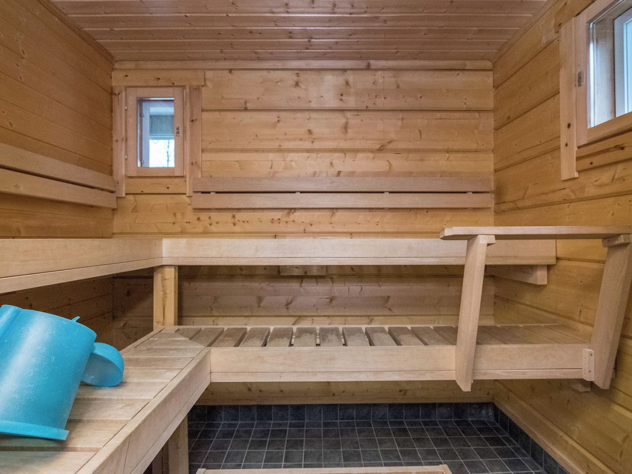 A wooden cabin interior with a bunk bed, a small window, and a blue bucket.