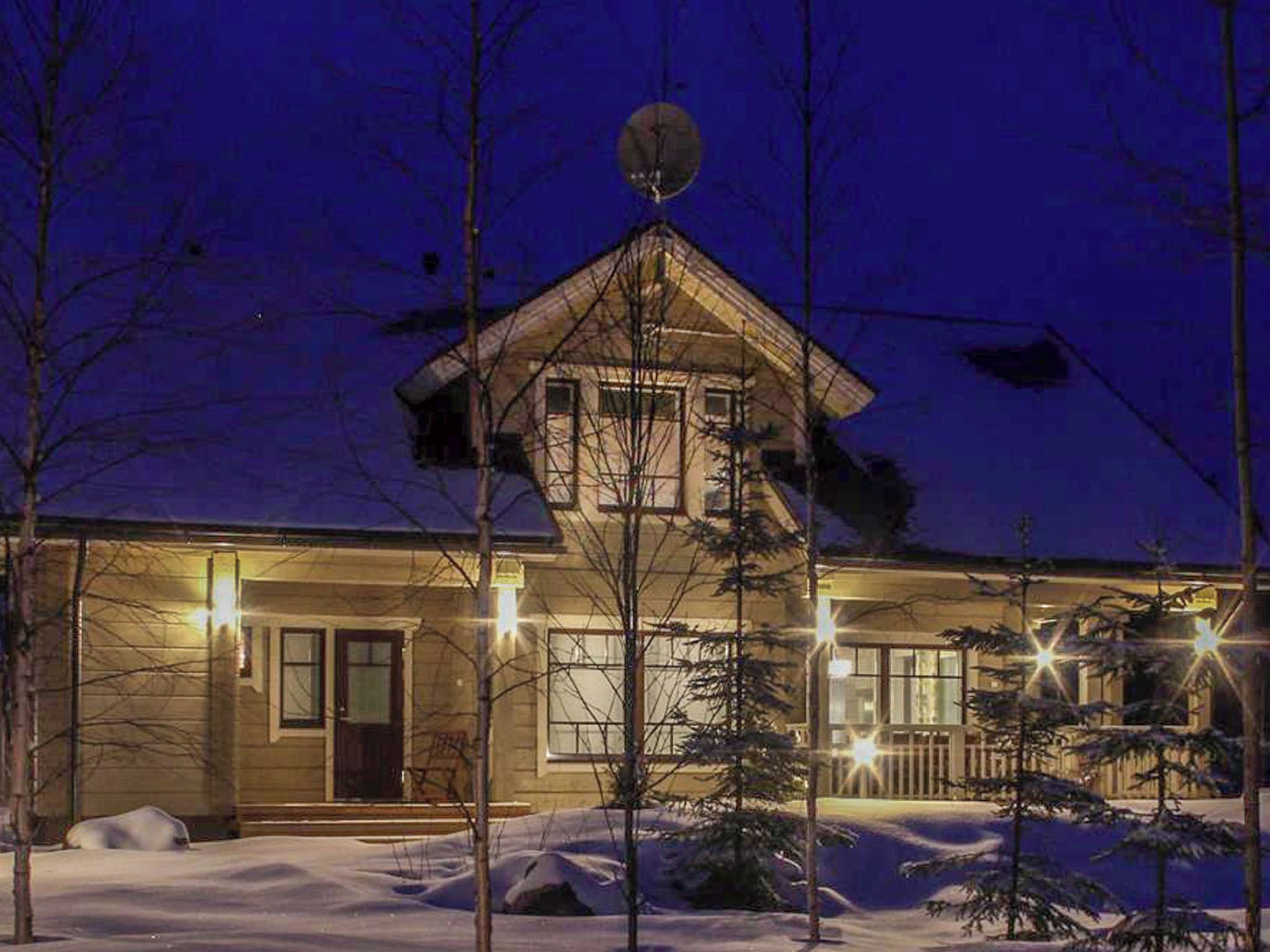 Una casa de dos pisos con techo inclinado, antena parabólica y un jardín delantero cubierto de nieve.