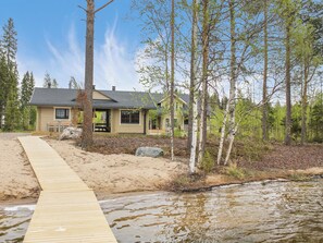 A house with a wooden deck leading to a sandy beach area.