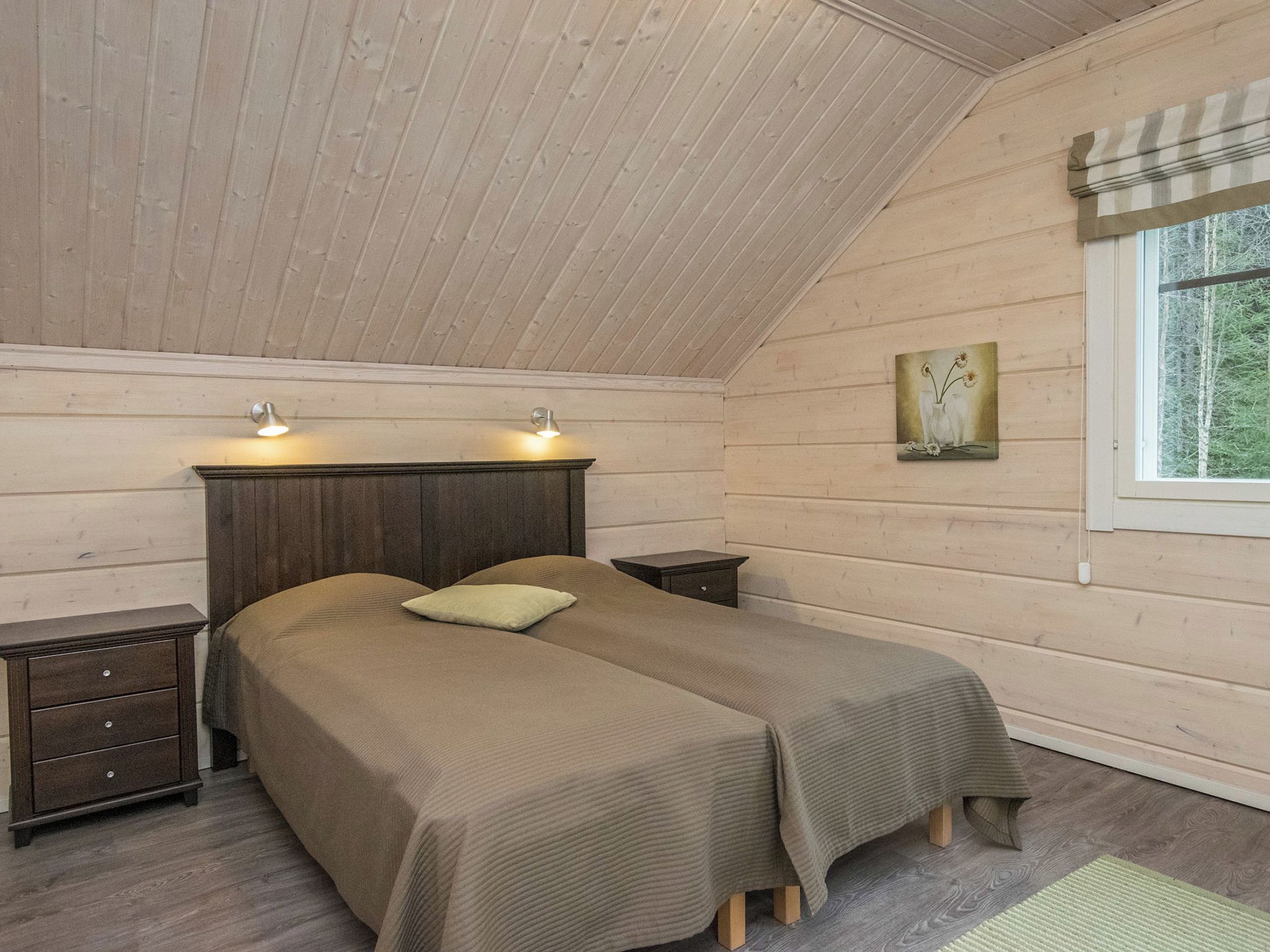 A bedroom with two beds, wooden walls, a window with a view, and a painting on the wall.