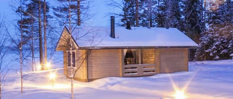 A cabin with a wooden exterior, a chimney, and a porch with a bench.