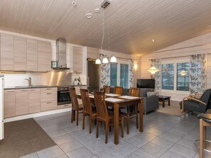 A modern kitchen with a dining area, a living room with a sofa and TV, and a ceiling with recessed lighting.