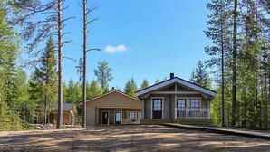 A two-story cabin with a front porch and a small attached shed, surrounded by trees and a body of water. - Villa mari by Interhome (Pertunmaa)
