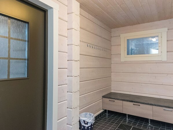 A laundry room with a door, a window, a bench, and a trash bin.