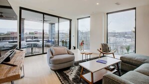 A spacious living area with large windows, a modern sofa, a coffee table, and a dining table. - Downtown C'ville Luxury w/ Rooftop Terrace (Charlottesville)