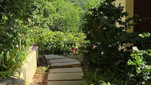 A stone staircase leading up to a building, surrounded by lush greenery and a view of a hillside with buildings in the distance.