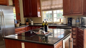 A kitchen with wooden cabinets, a stainless steel refrigerator, a large island with a black countertop, and a window with patterned curtains.