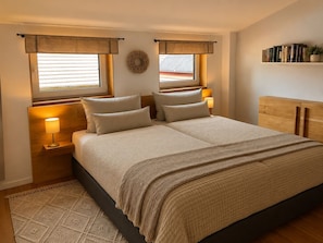 A bedroom with a bed, nightstands, a wall-mounted shelf with books, and a window with curtains. - Apartment Love - Refugium Lausitzer Seenland (Lauta)
