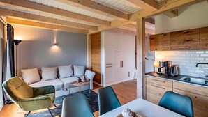 Un salon moderne comprenant un canapé, des fauteuils, une table basse et un coin cuisine avec un évier et un plan de travail.