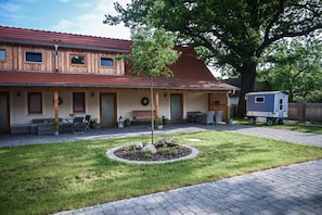 A two-story building with a covered patio area, a small tree in the center, and a trailer in the background.