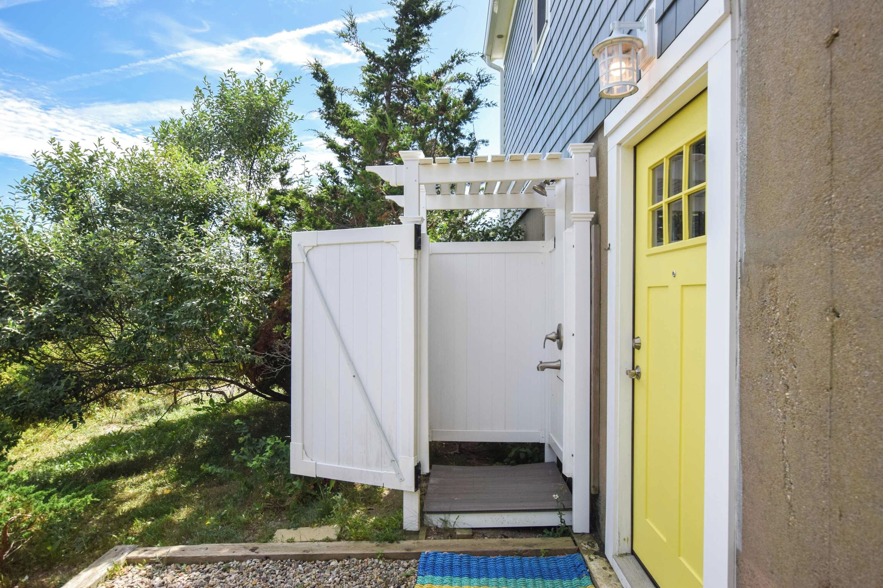 A white wooden gate leading to a porch with a yellow door.
