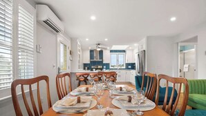 A dining area with a wooden table set for six, a kitchen in the background, and a green sofa.