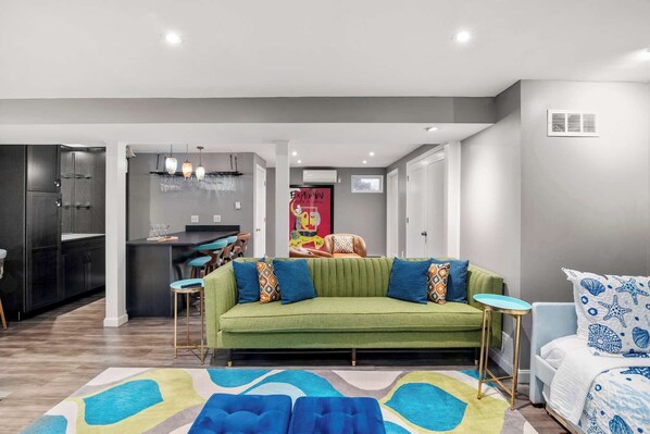 Een moderne woonkamer met een groene bank, een blauwe fauteuil met dessin en een kleurrijk vloerkleed.