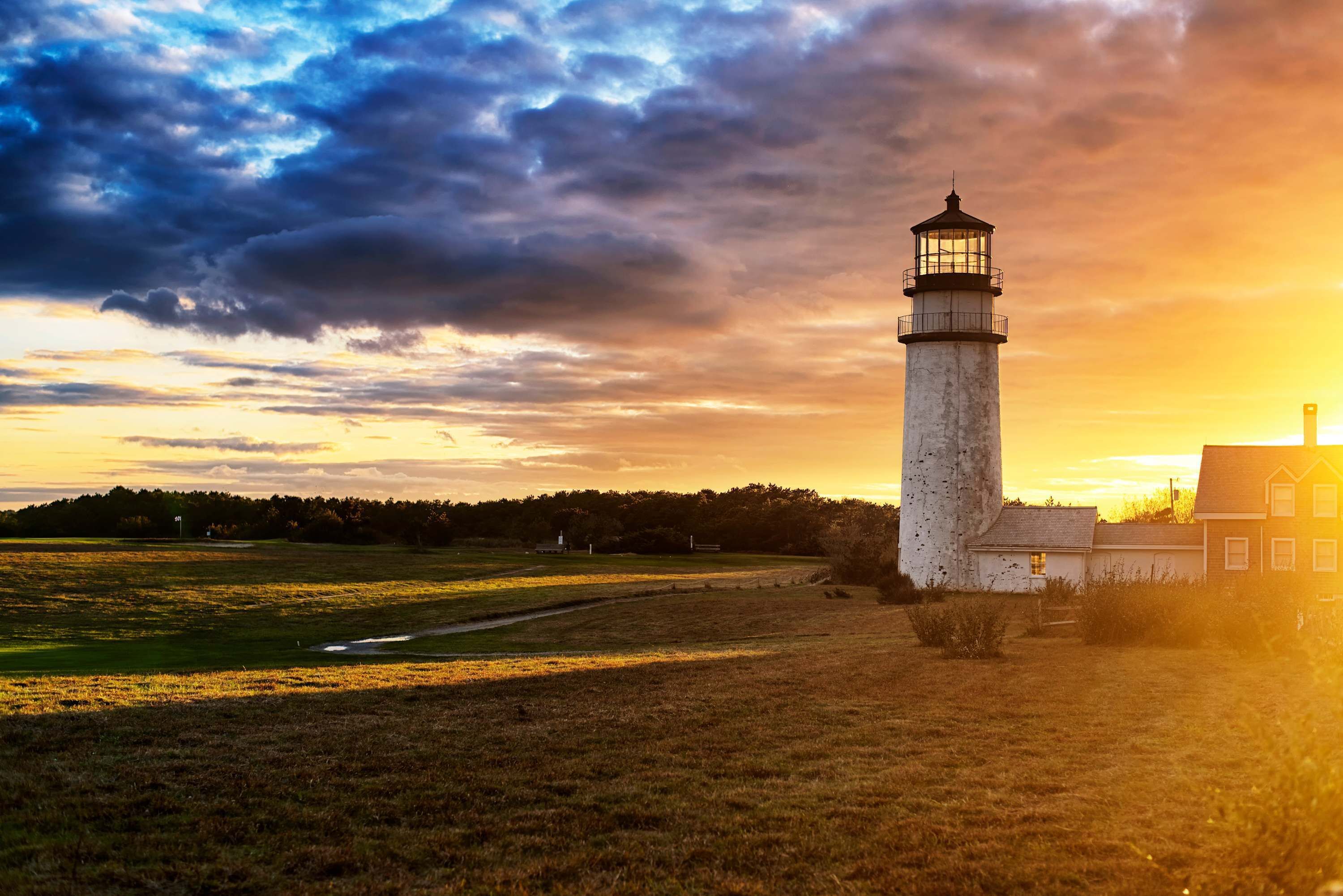 A lighthouse with a clear view of the surrounding landscape, including a path and a building in the foreground.