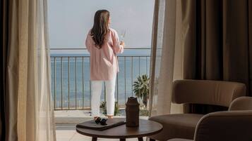 A room with a view of the sea, a balcony, a table with a vase, and a chair.