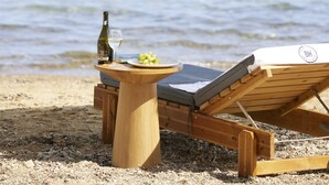 A wooden lounge chair and table with a bottle and grapes on a beach with a view of the sea. - Brown Beach Evia Island, a member of Brown Hotels (Eretria)