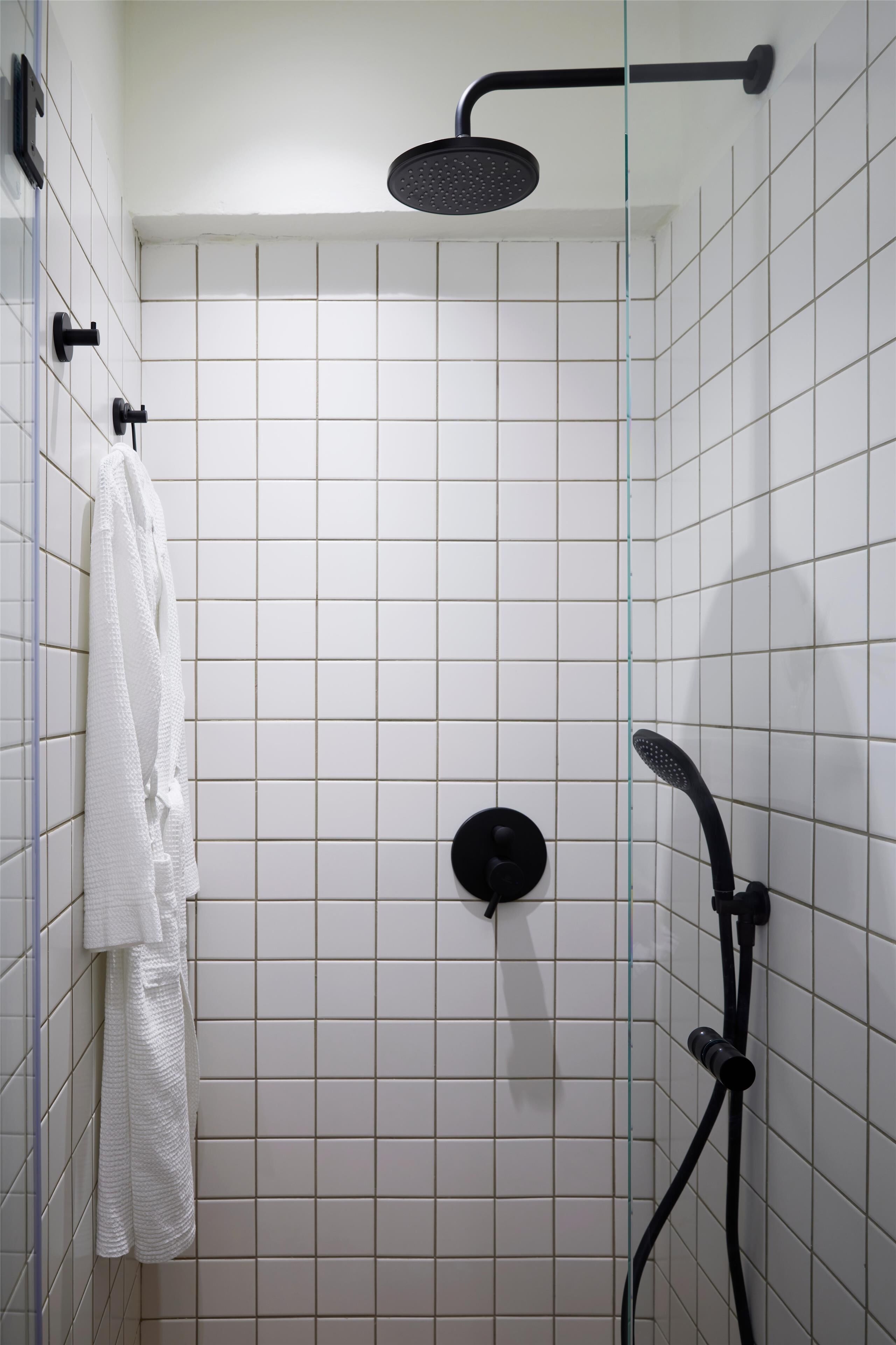 A shower area with white tiled walls, a white towel hanging on the wall, and a black showerhead.