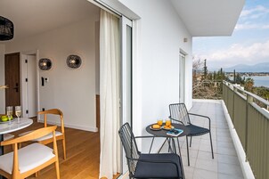 Un balcón con mesa para dos, una silla y vistas al mar y a las montañas.