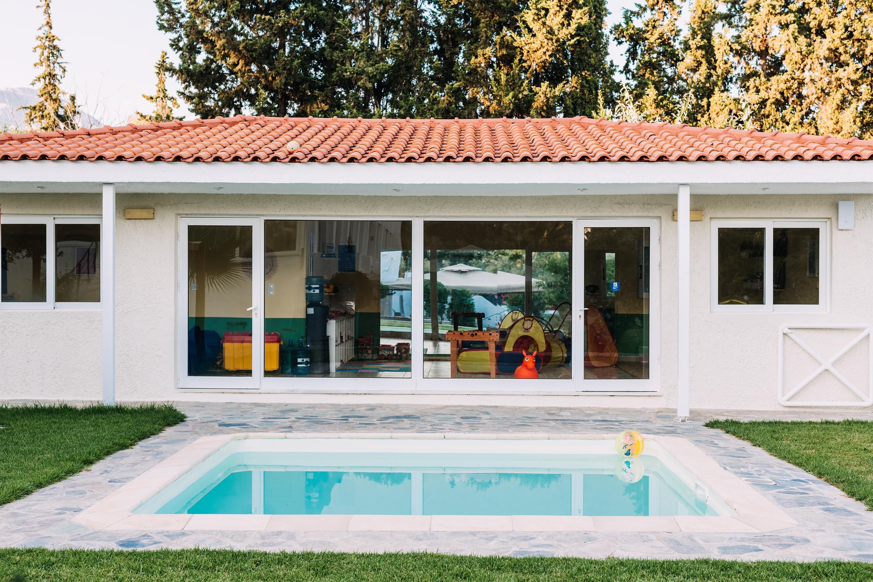 A house with a swimming pool, large windows, and a red-tiled roof.