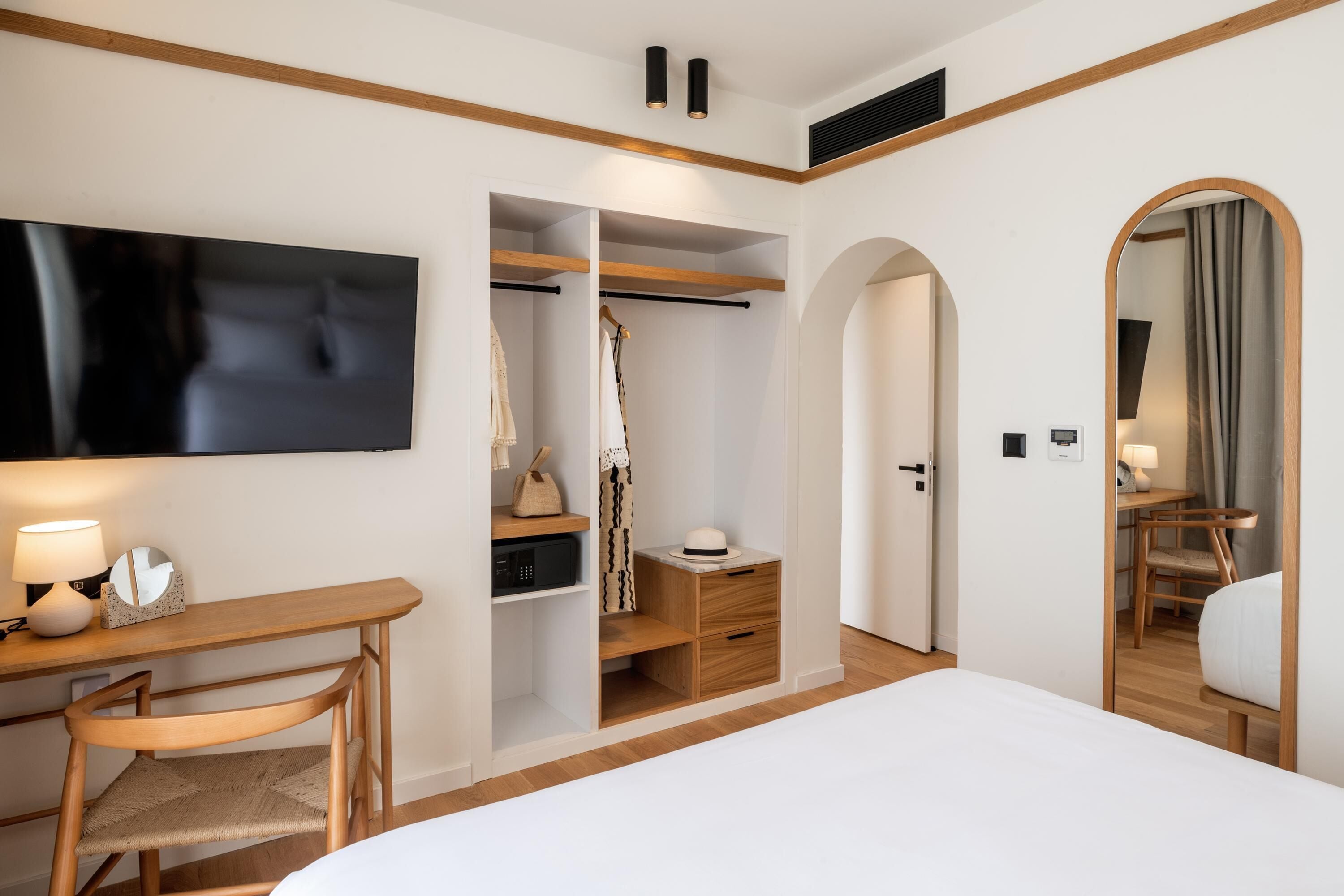 Ein Hotelzimmer mit einem Bett, einem Schreibtisch mit Stuhl, einem Kleiderschrank, einem Spiegel und einem Fernseher.