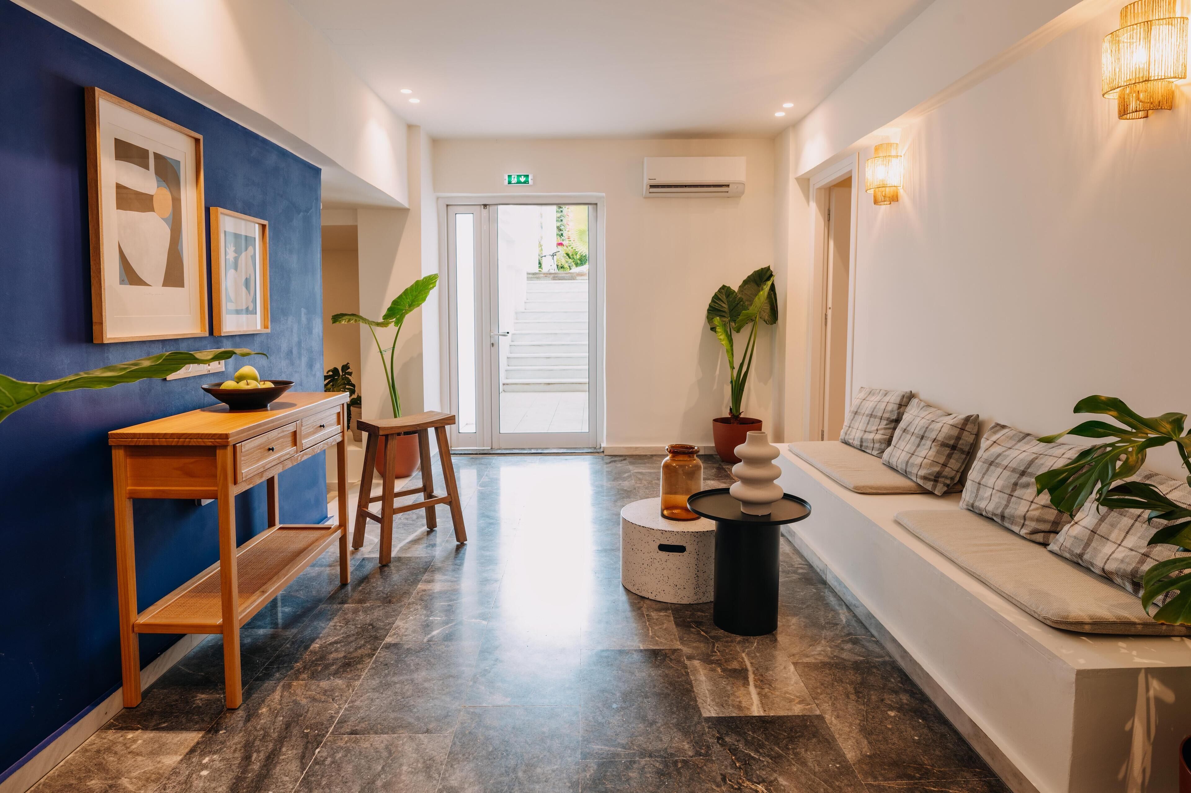 A modern hotel lobby with a blue accent wall, a wooden console table, a seating area with a sofa, and potted plants.