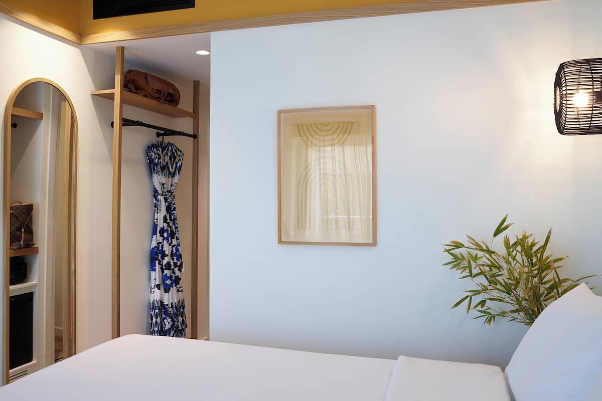 Ein Schlafzimmer mit einem Bett, einem Kleiderschrank, einem Spiegel, einem gerahmten Bild und einer Pflanze.
