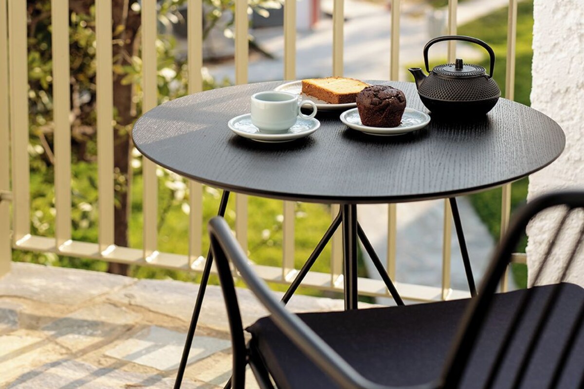 A round table with a teapot, a cup, and a muffin on a balcony with a railing.