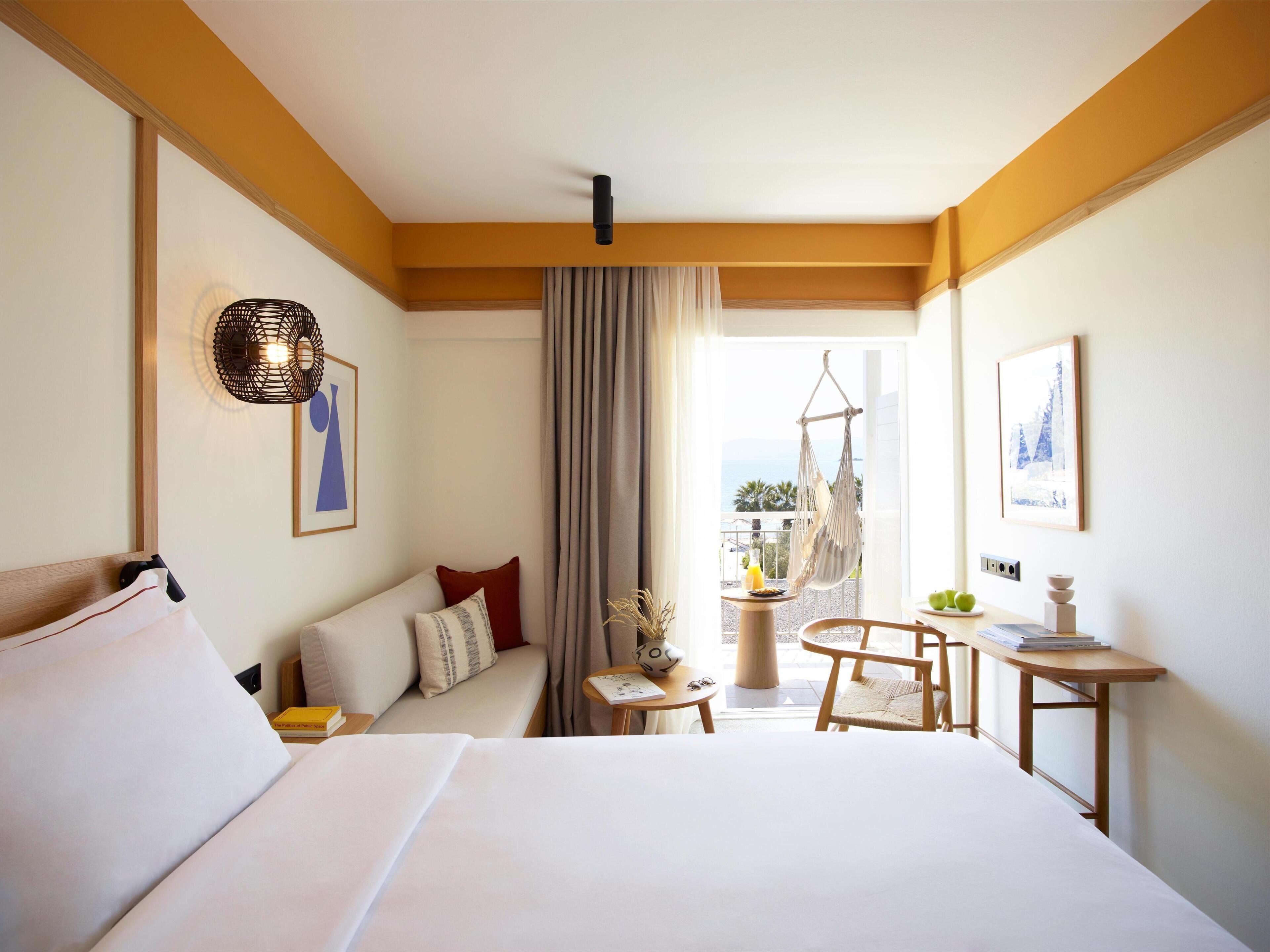 A hotel room with a bed, a seating area with a table and chairs, a hanging chair, and a balcony with a view.