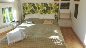 A neatly made bed with a green leaf-patterned headboard, a bedside table, and a window with curtains.