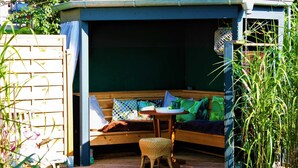 A cozy outdoor seating area with a wooden bench, a small table, and a wicker stool.