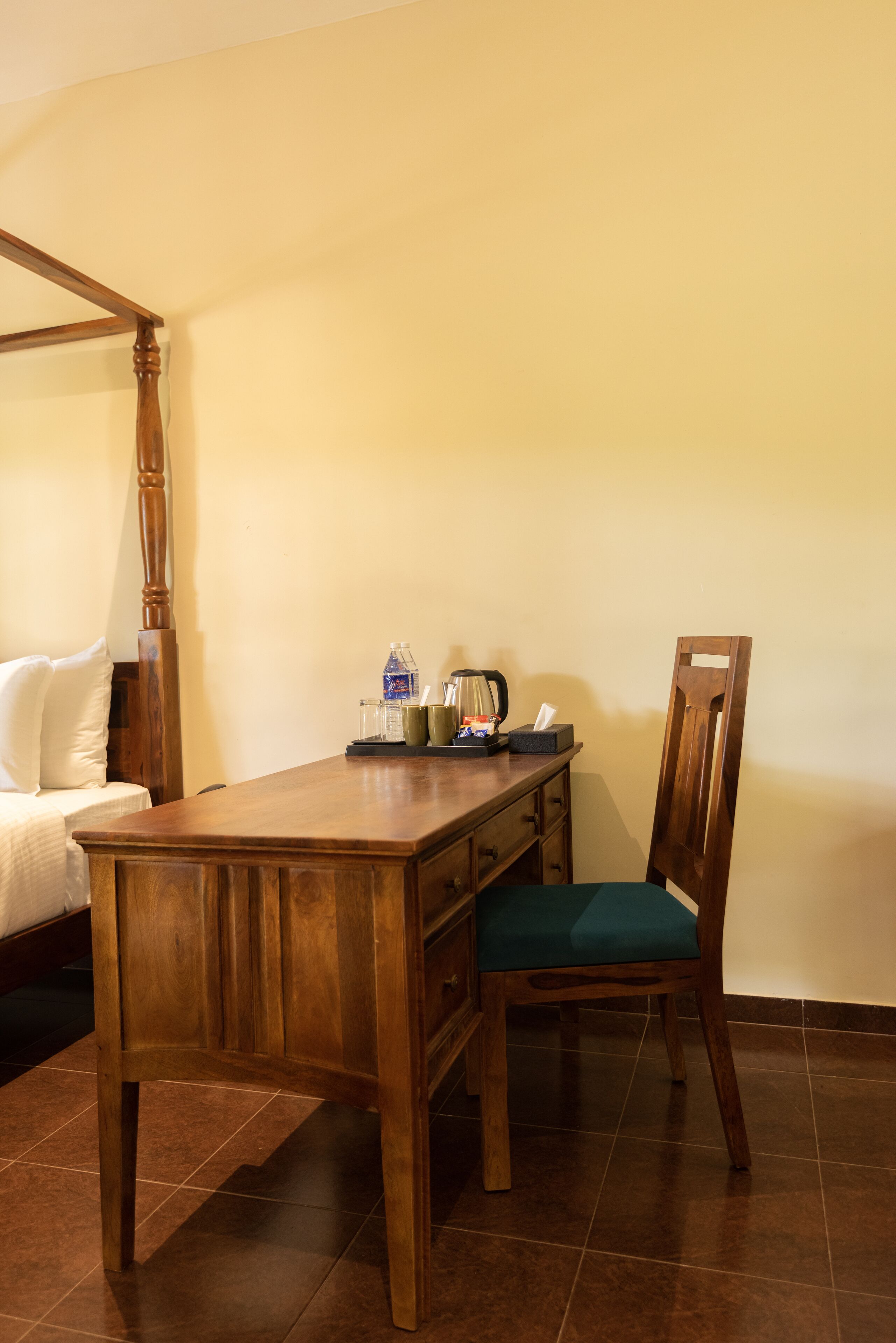 A wooden desk with a chair, a bedside table, and a bed with white linens.