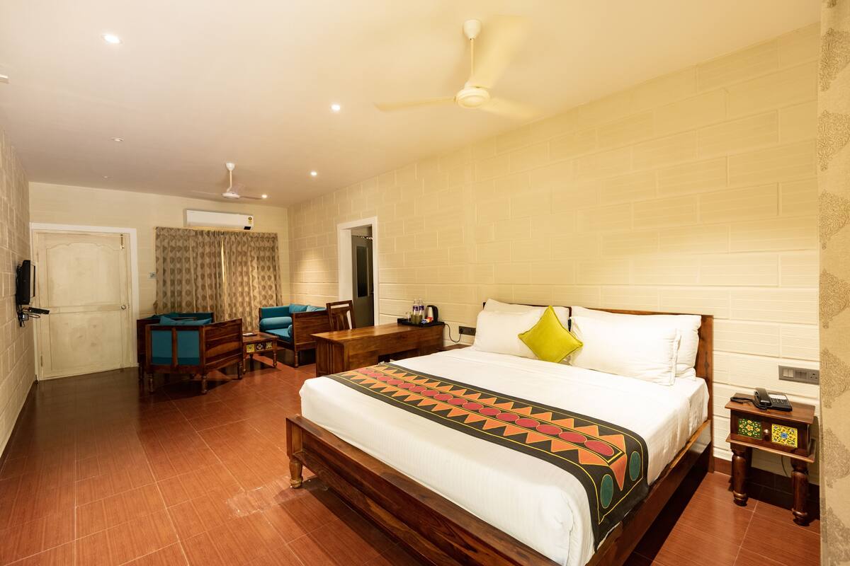 A hotel room with a large bed, a desk, a chair, a ceiling fan, and an air conditioning unit.