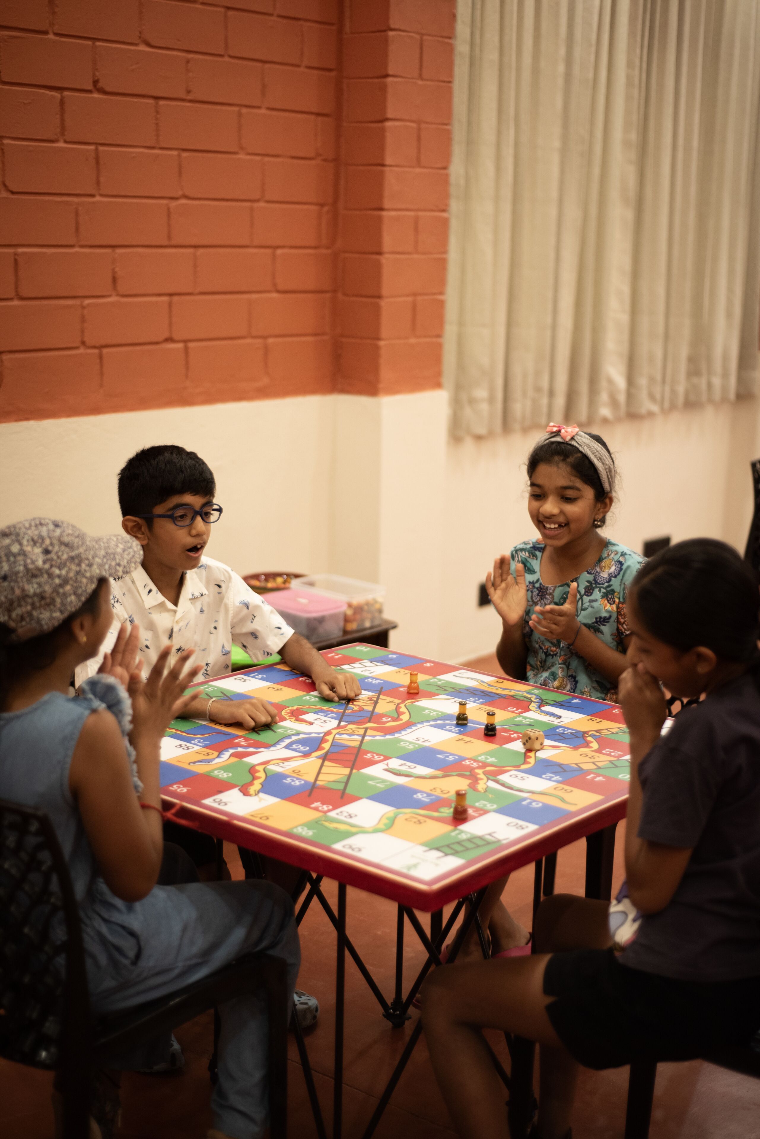 Un grupo de niños jugando a un juego de mesa en una habitación con paredes de ladrillo y una cortina.