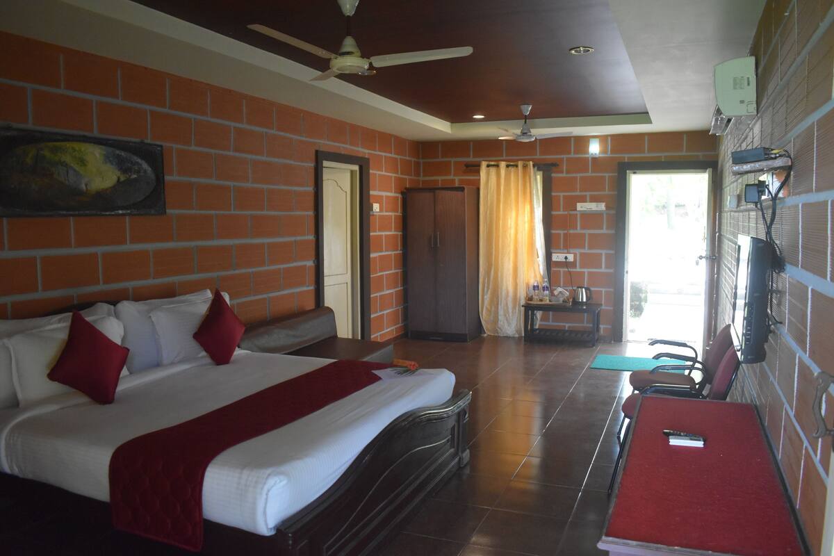 A hotel room with a bed, a desk, a chair, a ceiling fan, and a brick wall.