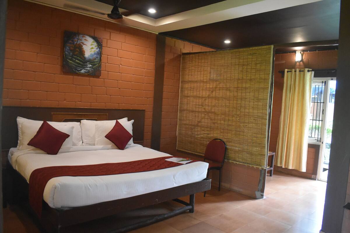 A hotel room with a large bed, a wooden headboard, a wall-mounted painting, a chair, and a window with curtains.