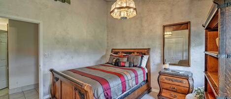 A bedroom with a wooden bed, a dresser, a mirror, and a hanging light fixture.