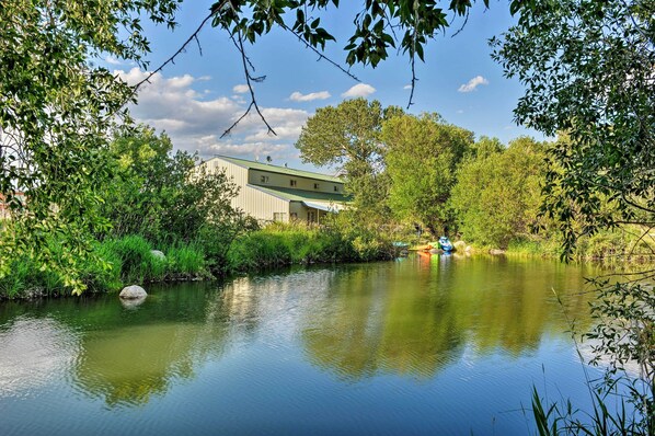 Vista al río con un edificio, abundante vegetación y una masa de agua tranquila.
