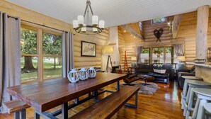Interior rústico de una cabaña con una mesa de comedor de madera, bancos, un sofá y una chimenea.